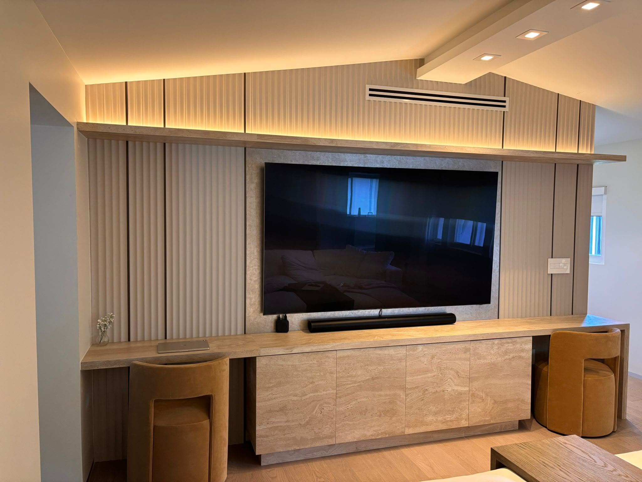 Completed television wall with integrated custom millwork, slatted surfaces, and lighting